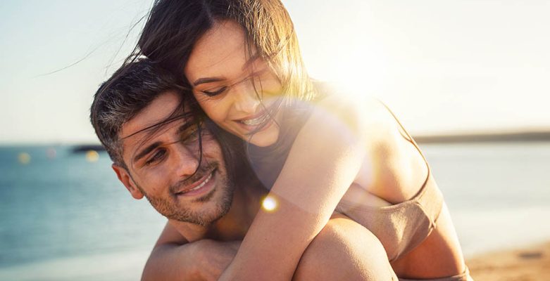 Junger Mann und junge Frau umarmen sich in Liebe an einem sonnigen Strand